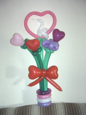 Five stems of love sprouting with hearts and flowers tied with a pretty balloon bow in a four color pot!